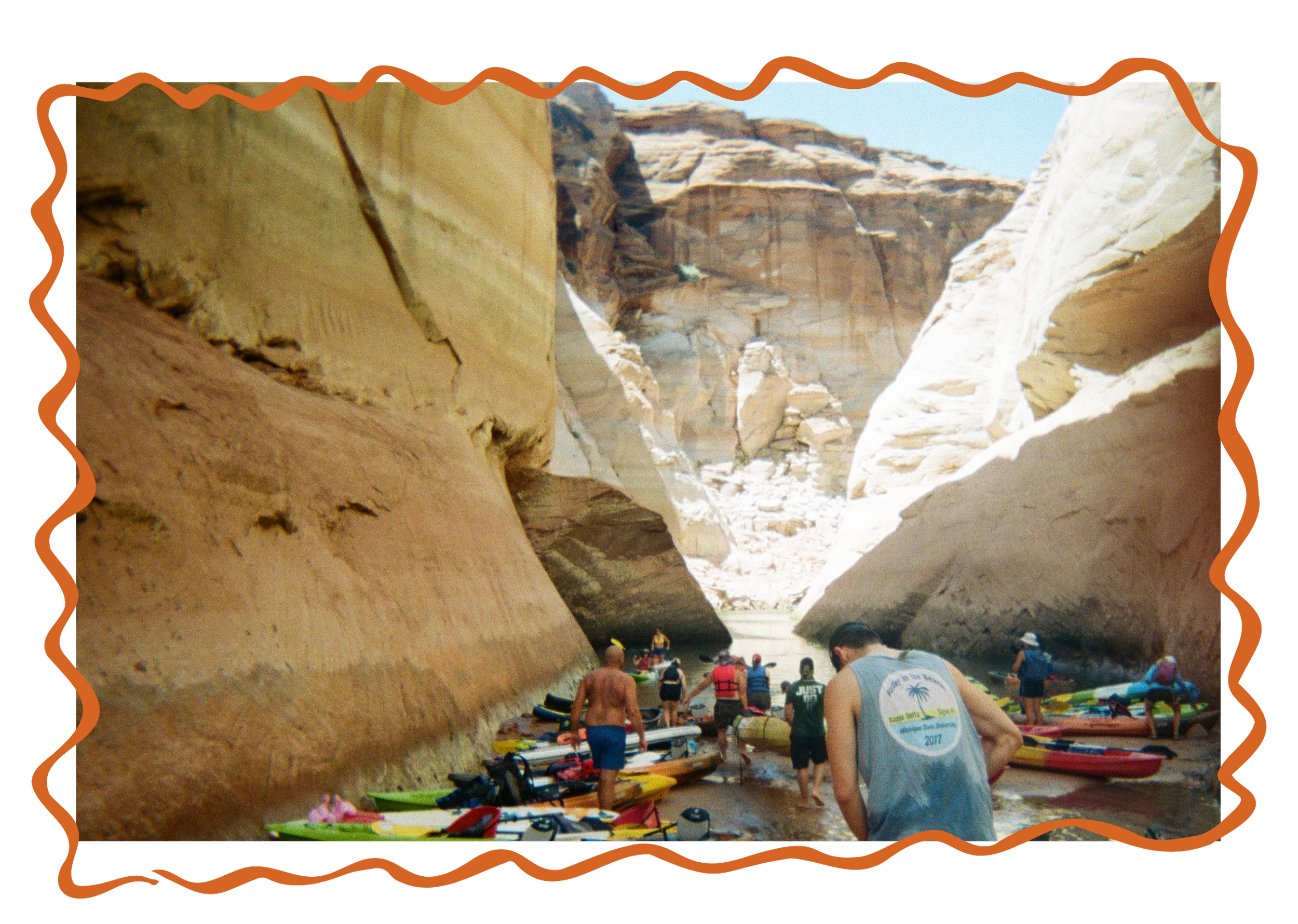 Group of people kayaking and preparing their kayaks in a narrow slot canyon with steep, towering sandstone walls on a sunny day.
