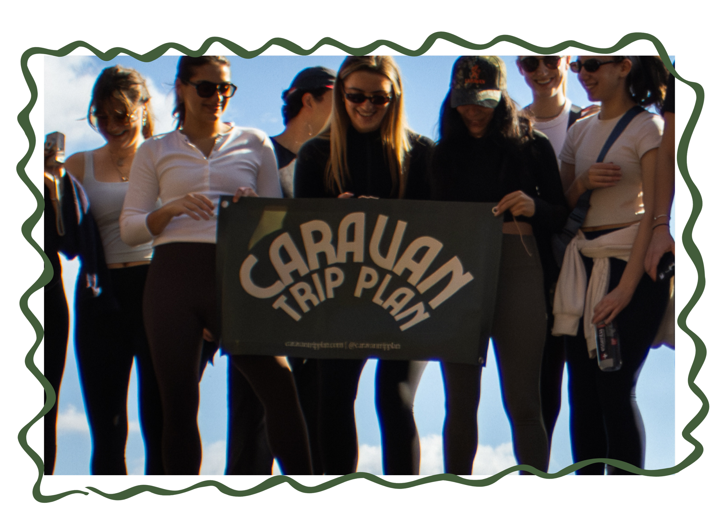 Group of women holding a sign that reads 'Caravan Trip Plot' outdoors on a sunny day, with a clear blue sky in the background.