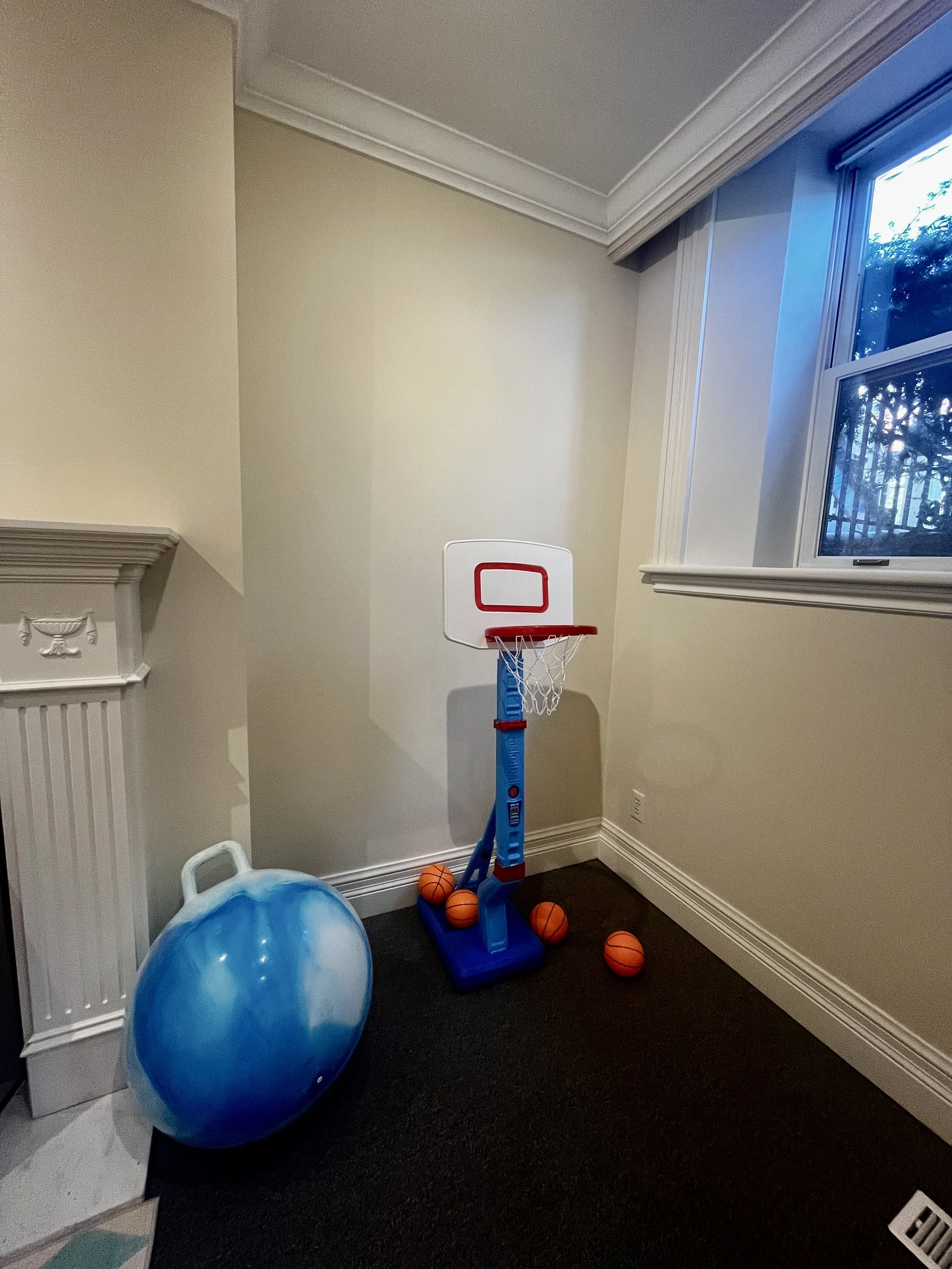 Indoor corner with a small portable basketball hoop, four mini basketballs, and a blue exercise ball