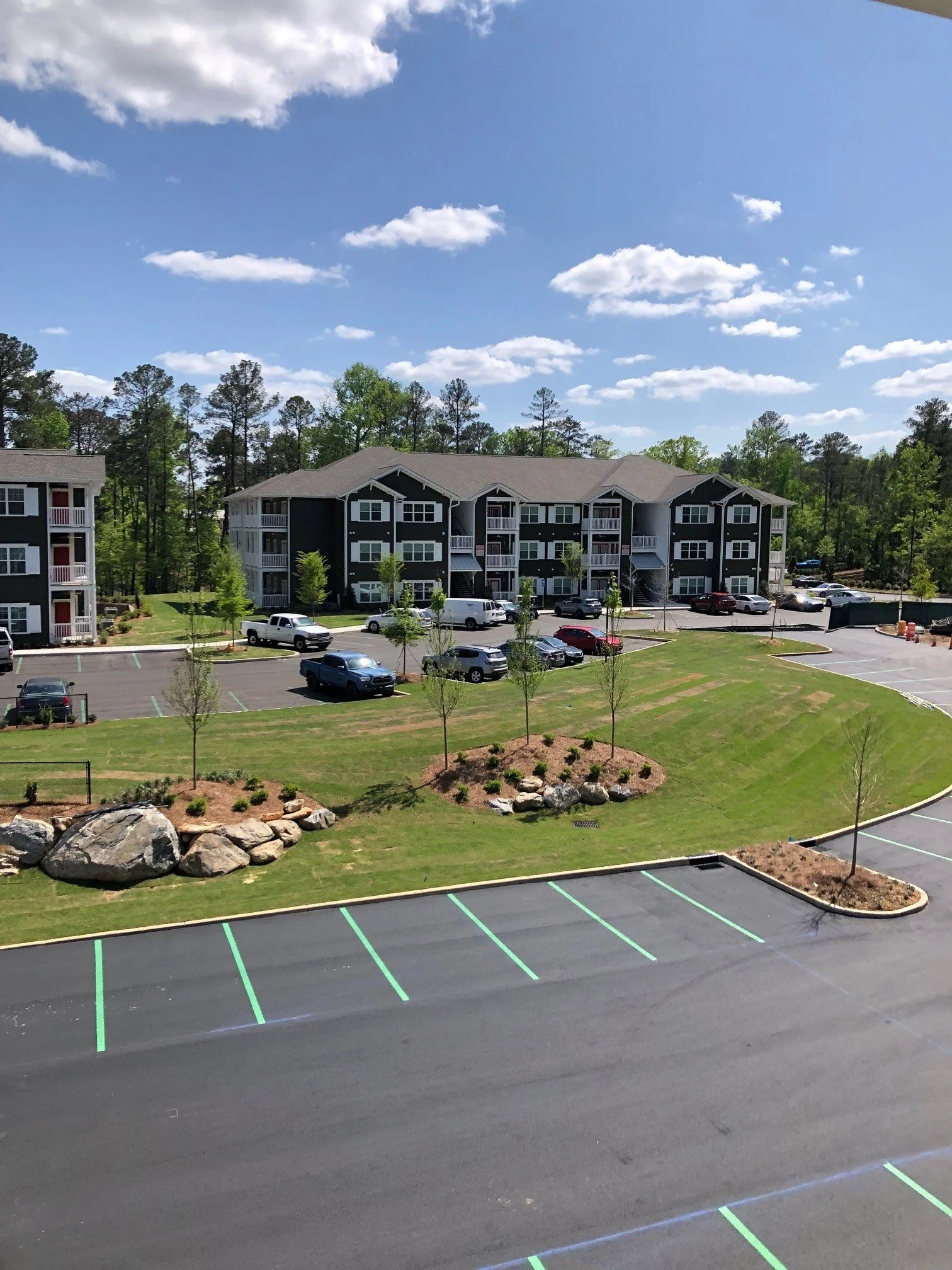 Parking lot with some saplings and a few apartment buildings in the Swallowtail Flats multifamily apartment complex - Columbus, GA