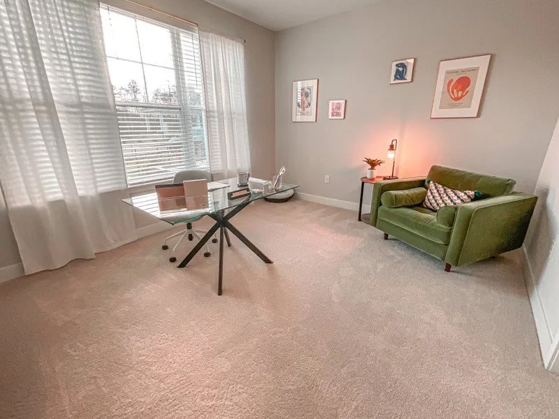Office room with a large window, corner chair, and glass working table within the Courtney Ridge multifamily apartment complex - Charlotte, NC