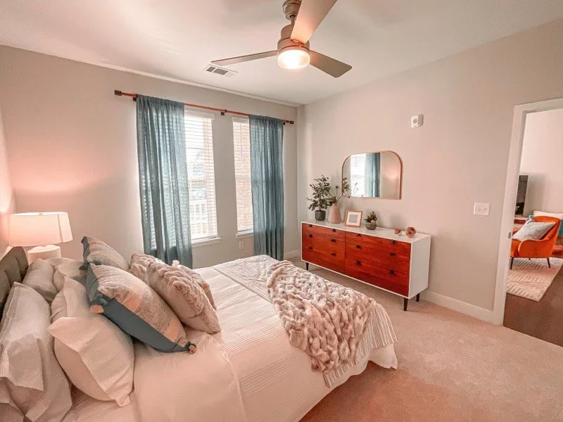 Bedroom with a large, sunny window, blue curtains and colorful, modern dresser within a typical unit in the Courtney Ridge multifamily apartment complex - Charlotte, NC