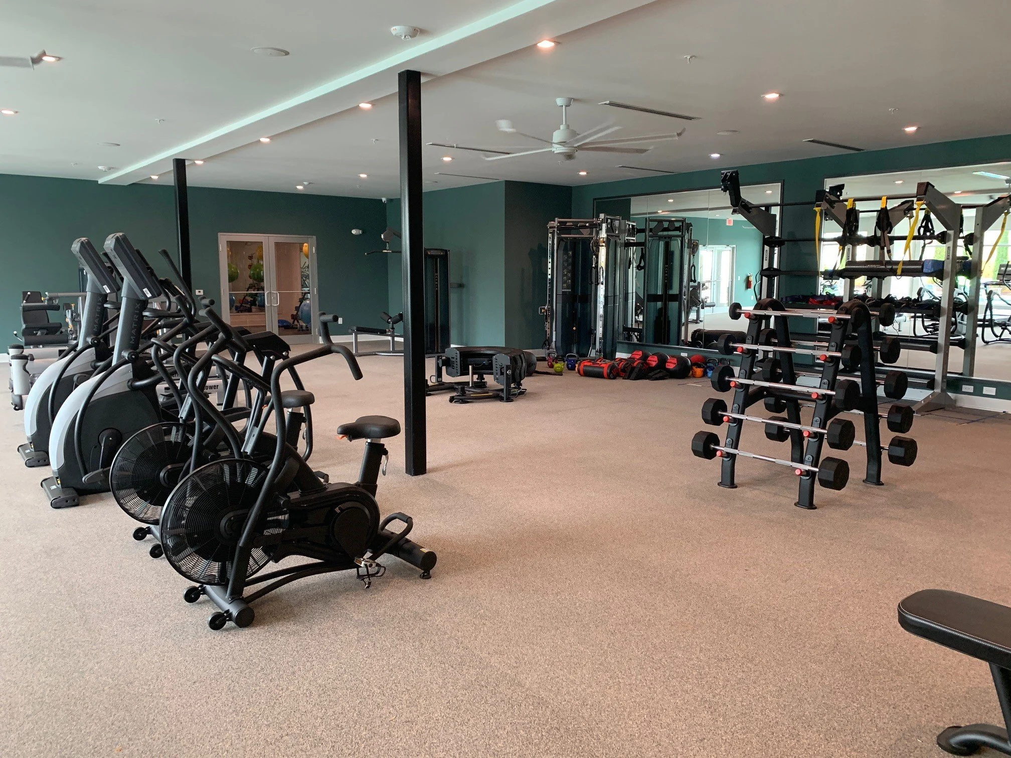 Indoor gym with cardio machines, weights, and a large mirror located within The Beacon - Kennesaw, GA