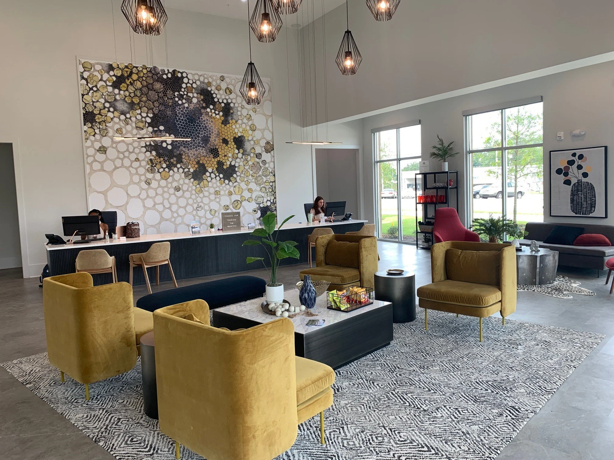 Seating area with a large abstract wall panting and four yellow chairs located in the common room at The Beacon - Kennesaw, GA