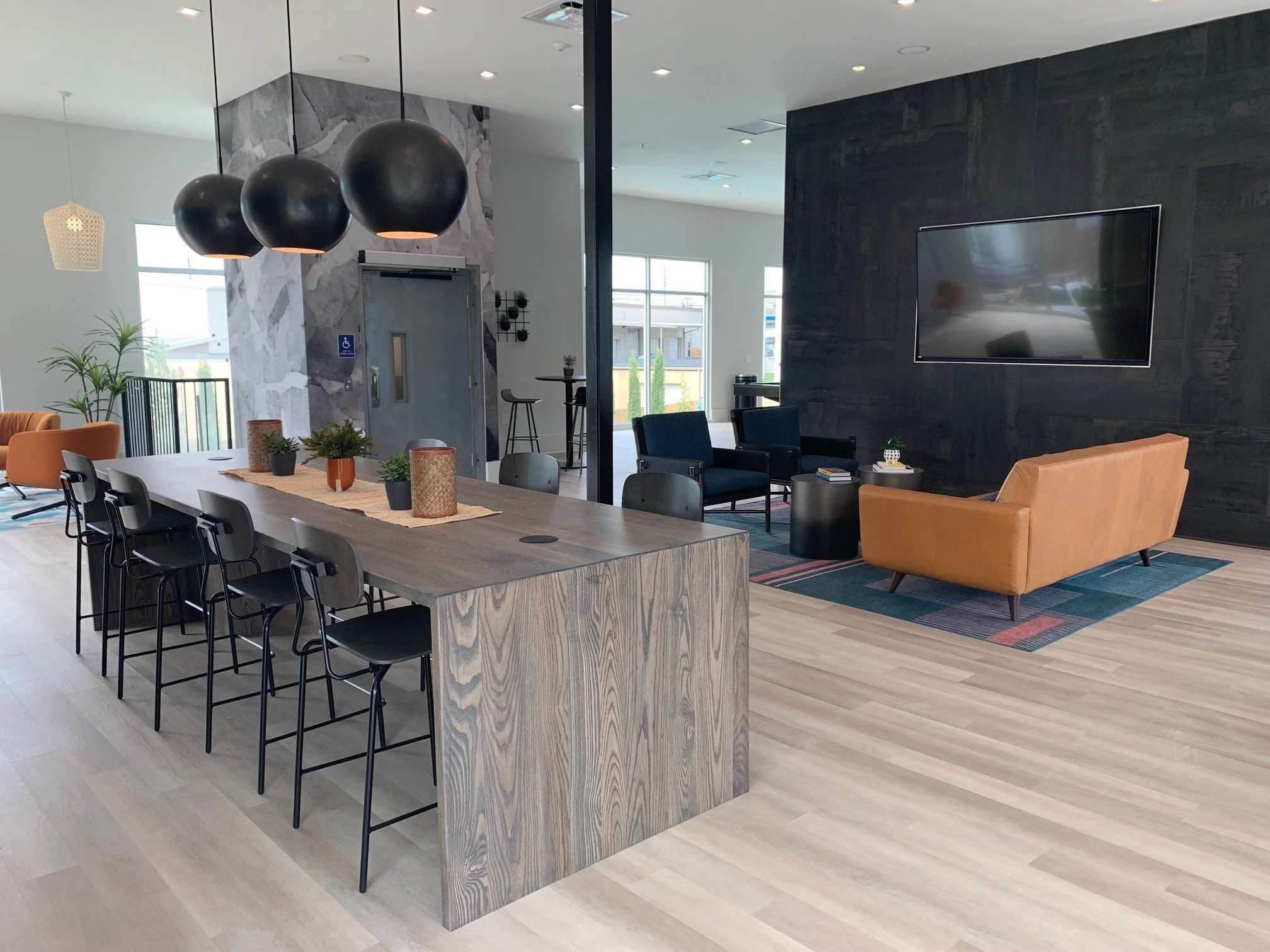 High-top bar table and seating area with a wall-mounted TV and wood floors, located in the common room at The Beacon - Kennesaw, GA