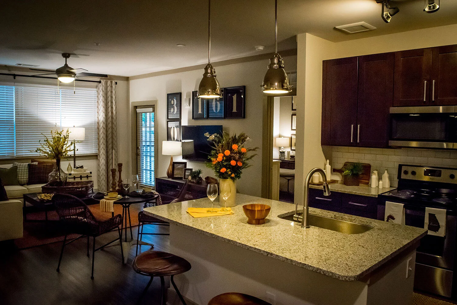 Typical kitchen with an island, some barstools, and the living room with a wall-mounted monitor in the background at the Riverpoint - Rome, GA