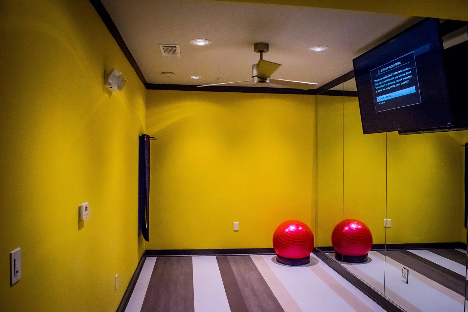 Workout room with a yellow wall, large mirrors, a TV monitor, and a stability ball at the Riverpoint - Rome, GA