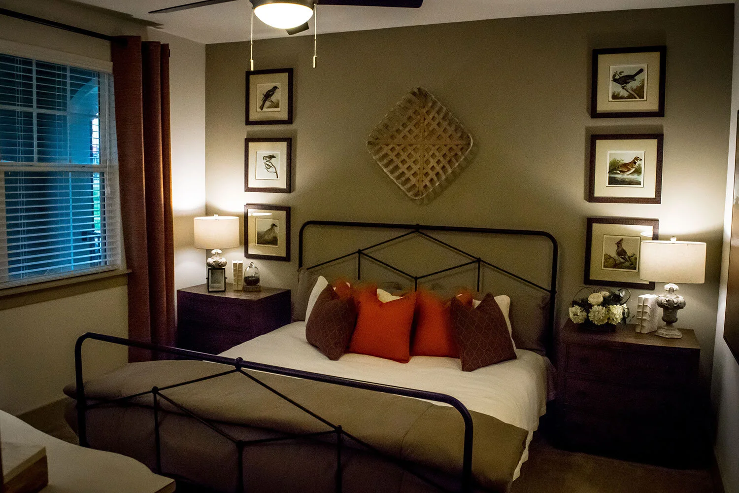Typical bedroom found in a multifamily apartment building with matching sage green duvet and walls and red pillows with various pieces of wall art seen at Riverpoint - Rome, GA