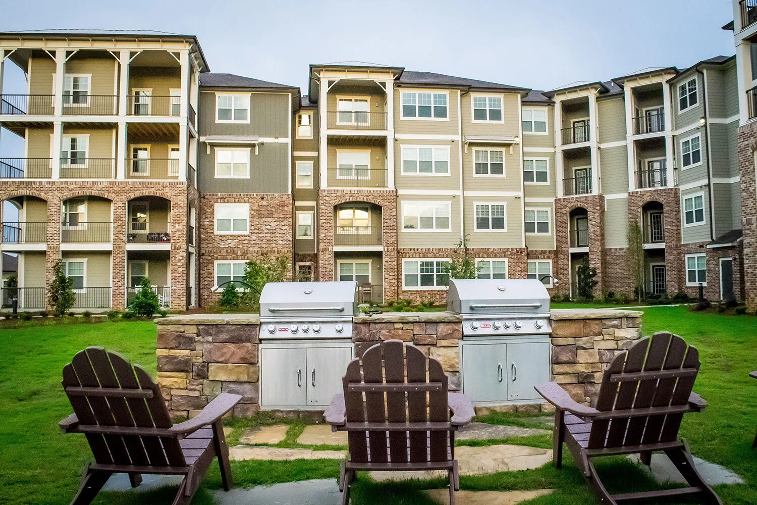 Low-angle shot of multifamily apartment complex units with grills and Adirondack chairs out front at the Riverpoint - Rome, GA
