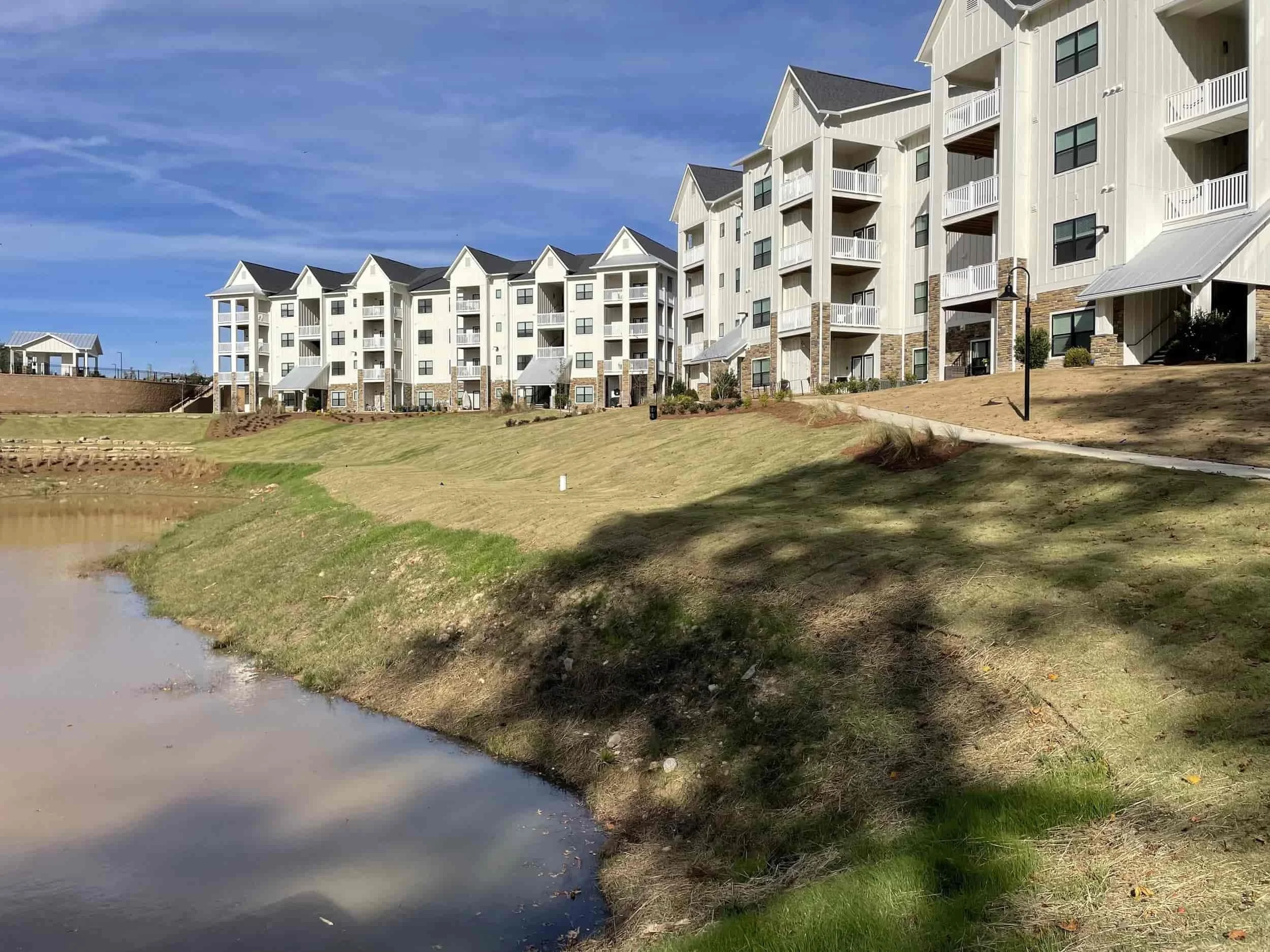 Row of apartments next to a walking path, green space and pond.