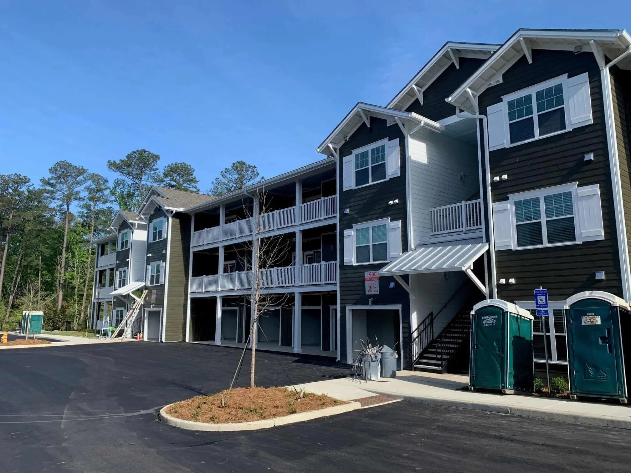 New multi-story apartment building with black and white siding, several balconies, and accessible parking spaces in the foreground. Trees are in the background.
