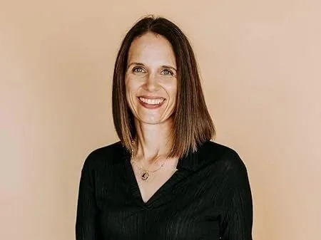 A woman with shoulder-length brown hair smiling against a beige background.