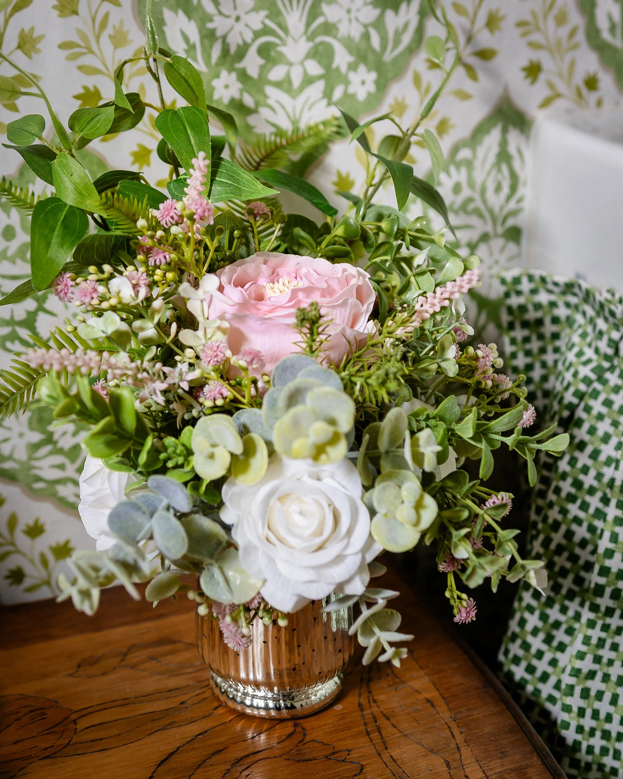 A bouquet of pink, white, and green flowers in a glass vase on a wooden table. Designed by Flower Fauxnatic.