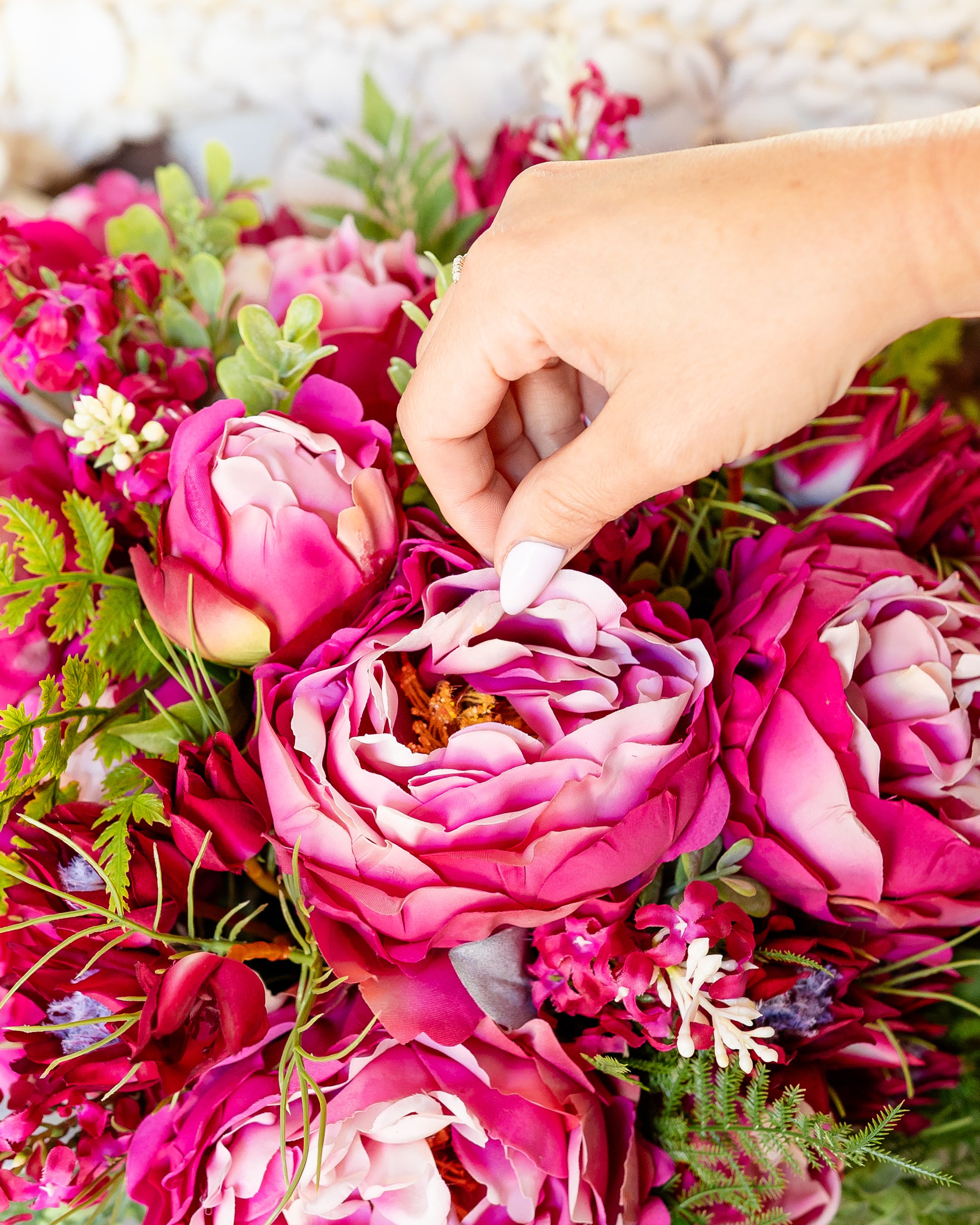 A hand with white nail polish is picking up a butterfly from a bouquet of pink, purple, and white flowers. Designed by Flower Fauxnatic.