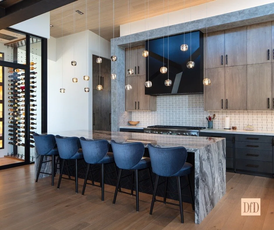 Where modern warmth meets statement design. 🍷✨

From the waterfall stone island to the sculptural pendants and deep blue seating, this kitchen balances bold materials with effortless functionality. With a wine wall that turns storage into art, it&rs