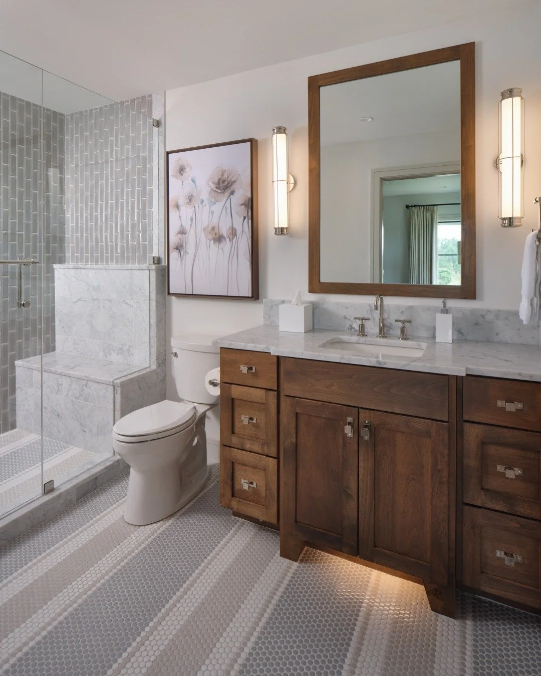 Proof that simple does not have to mean expected.

In this bathroom, a playful striped penny round tile floor adds movement and personality, elevating an otherwise simple foundation. Though grounded in cool grey marble and tiles, the warmth of the st