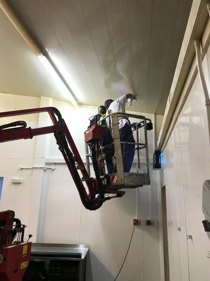 Two workers on a lift inspecting or repairing the ceiling of a room with one person wiping the ceiling.