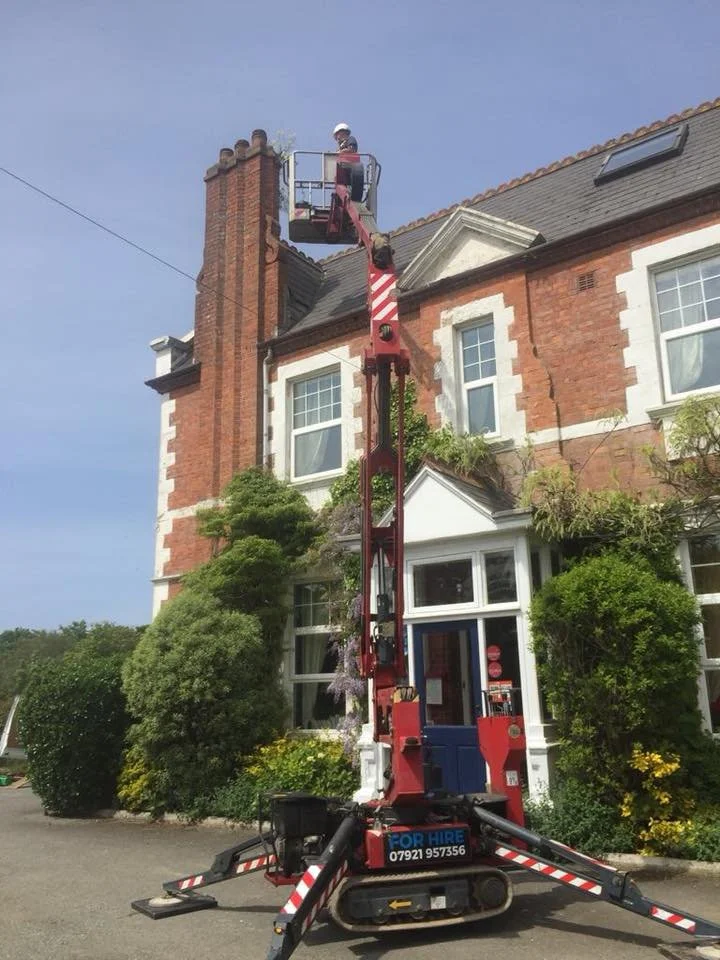 A worker in a bucket lift trims a chimney on a brick house.