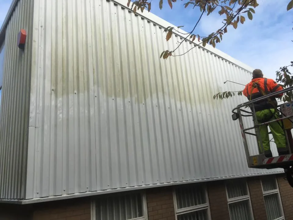 A worker on a lift painting or cleaning the exterior wall of a building.
