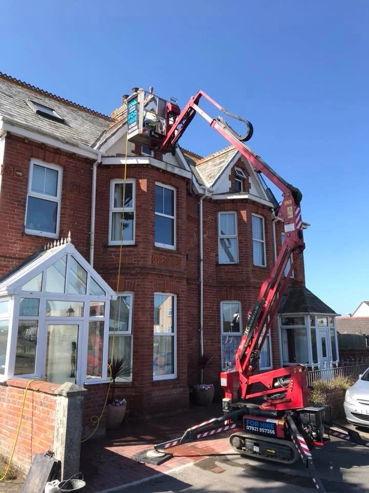 Construction workers using a hydraulic lift to access the roof of a brick house for repairs or maintenance.
