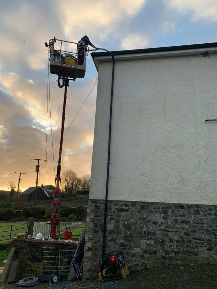 A worker in a lift working on the roof of a house during sunset, with tools and equipment nearby.