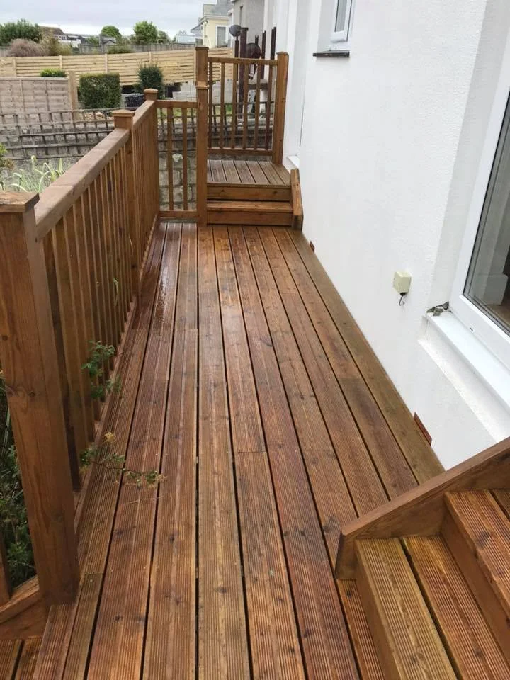 Clean, wet wooden deck with stairs leading up to a small fenced area with garden plants in a backyard.