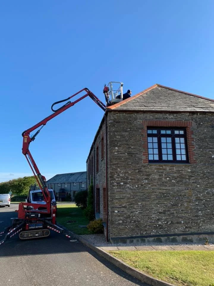 A truck with a boom lift extending to the roof of a brick building, where two workers are inspecting or repairing the roof under a clear blue sky.