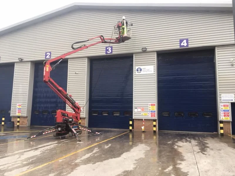 A worker on a cherry picker working on the exterior of a warehouse with numbered garage doors.