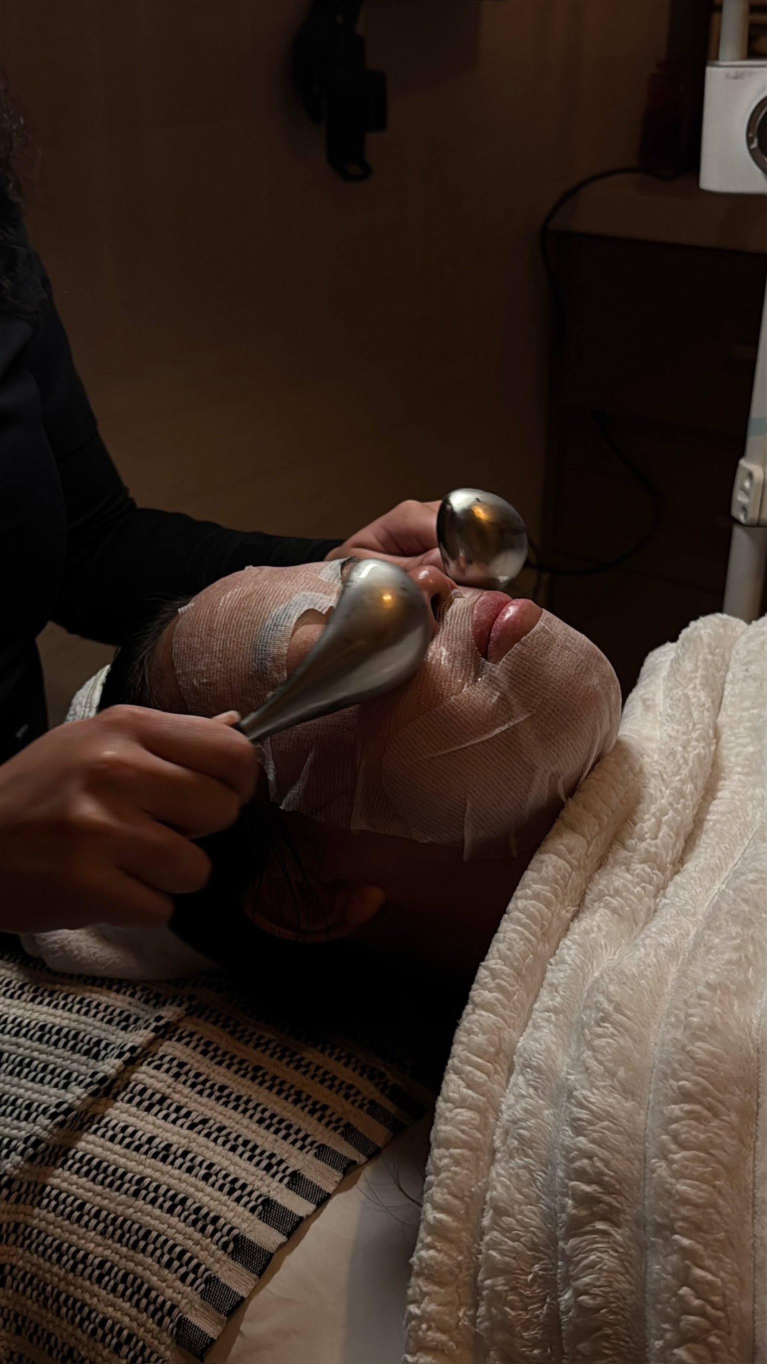 Client with sheet mask and cooling globes to soothe, depuff, and enhance facial results.