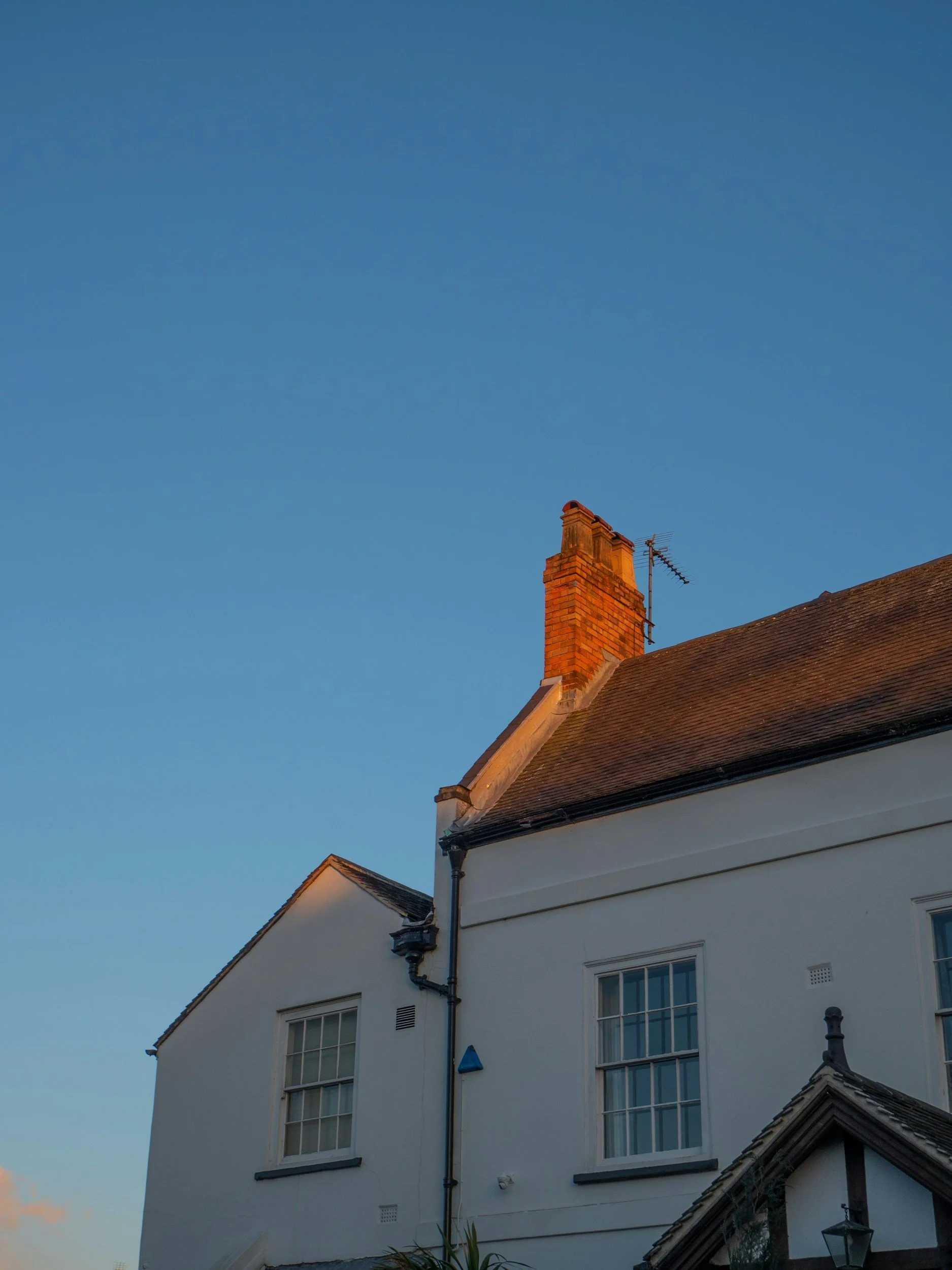 White house with a brick chimney under a clear blue sky, with some windows and roof details visible.
