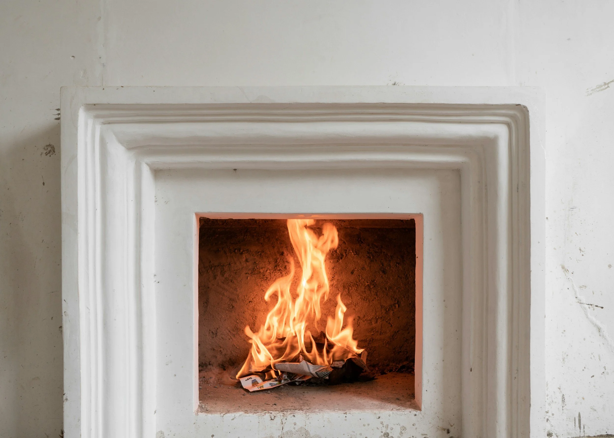 Fire burning inside a small fireplace with a white mantel over a white wall.