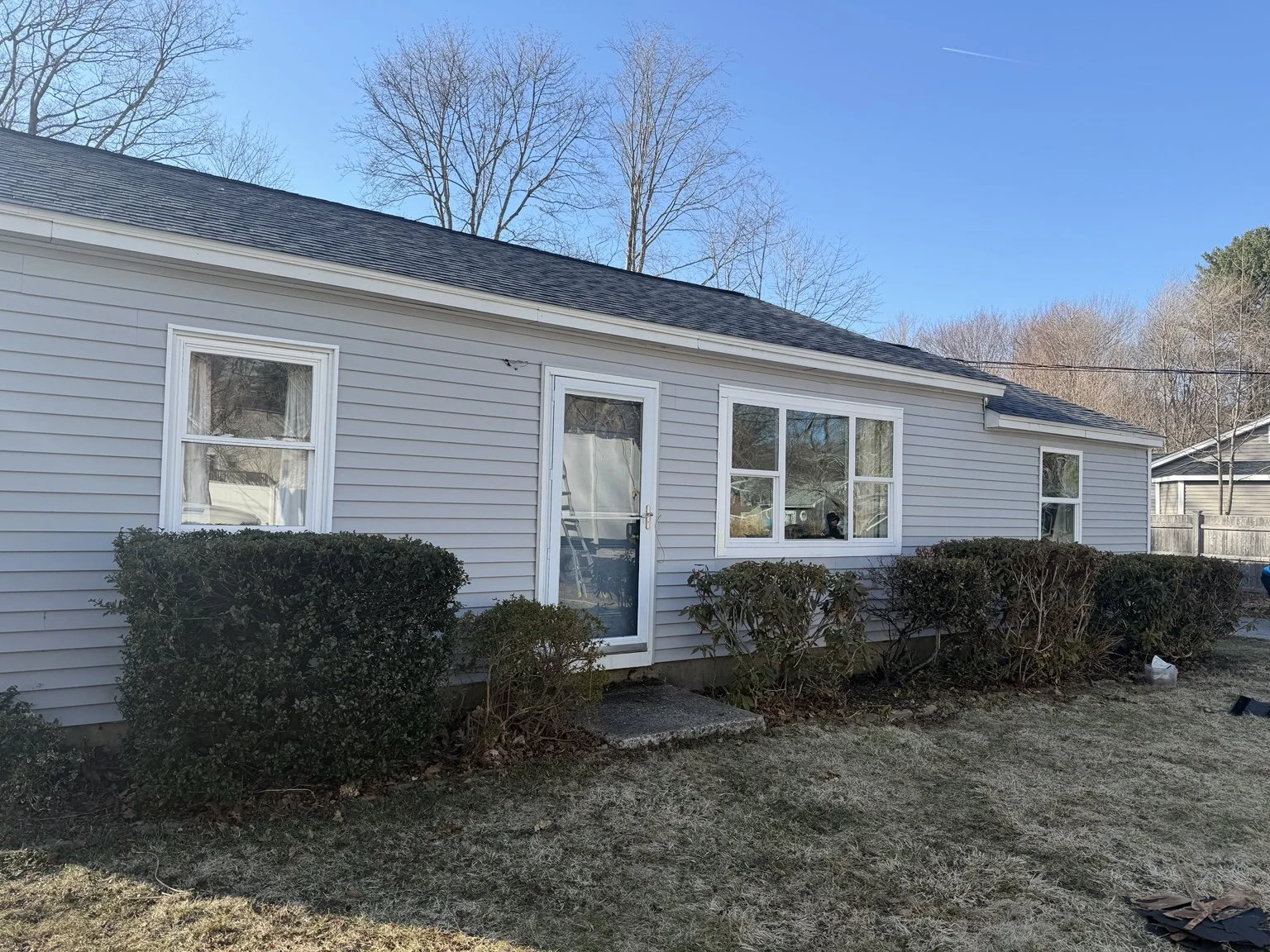 Completed light-gray siding installation with finished windows, trim, and front entry.