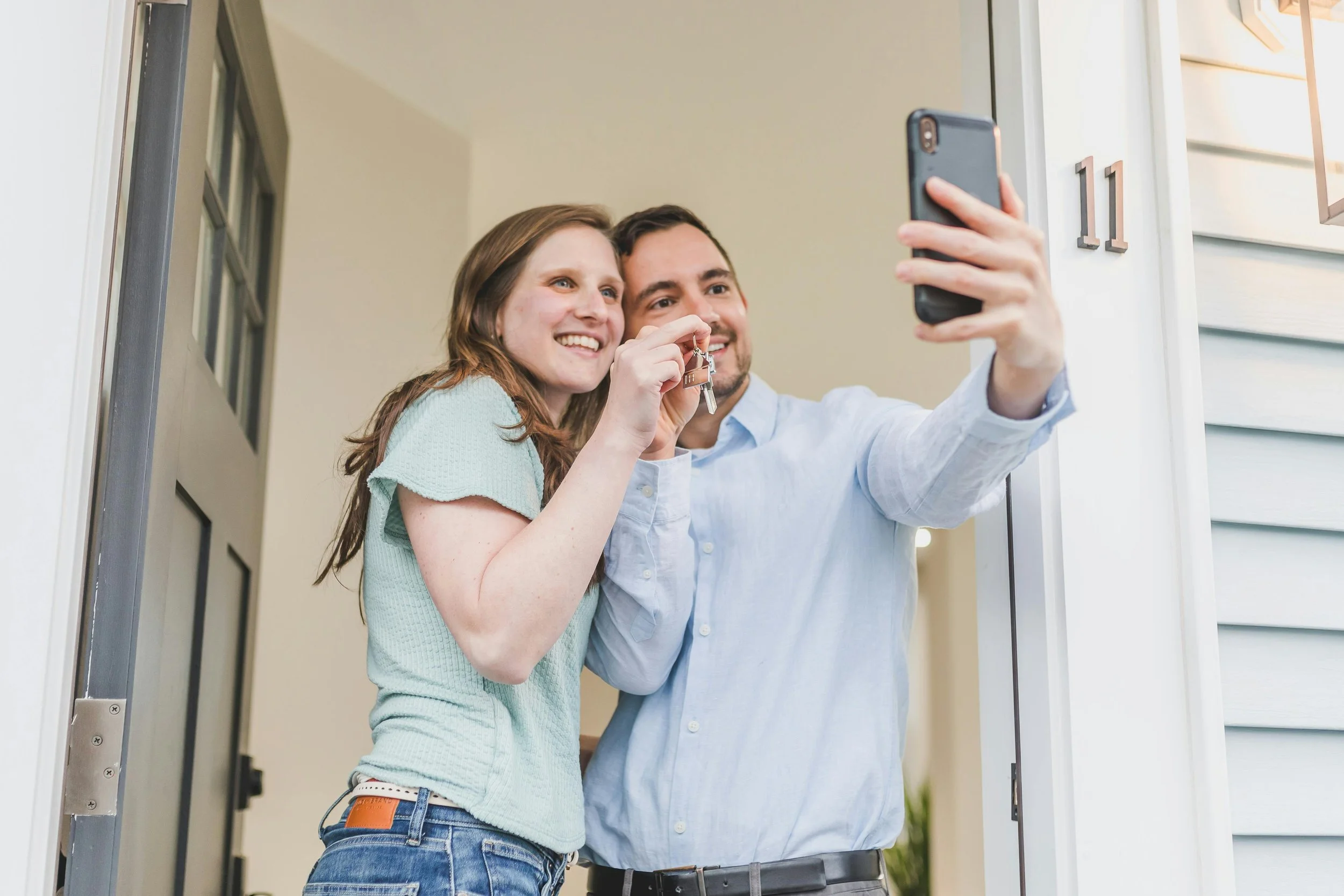 A happy couple takes a selfie at the doorway of their new home, proudly holding up the house keys. Reflecting the perspective of Ryan Weible San Ramon on how to navigate the first-time homebuyer process with confidence.