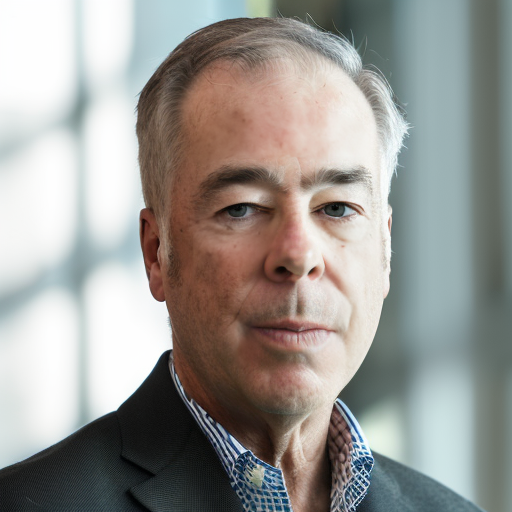 Close-up portrait of a middle-aged man with gray hair and blue eyes, wearing a dark suit and a light blue shirt, standing indoors with blurred windows in the background.