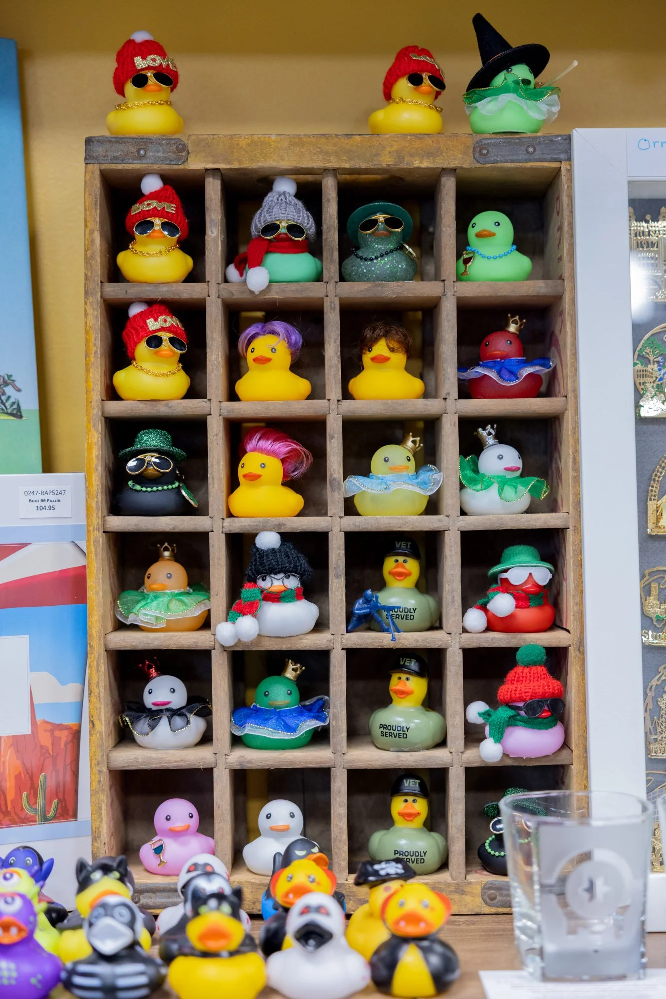 A display of rubber duckies dressed in Christmas costumes, some with sunglasses, hats, and accessories, arranged in a wooden cubby shelf.
