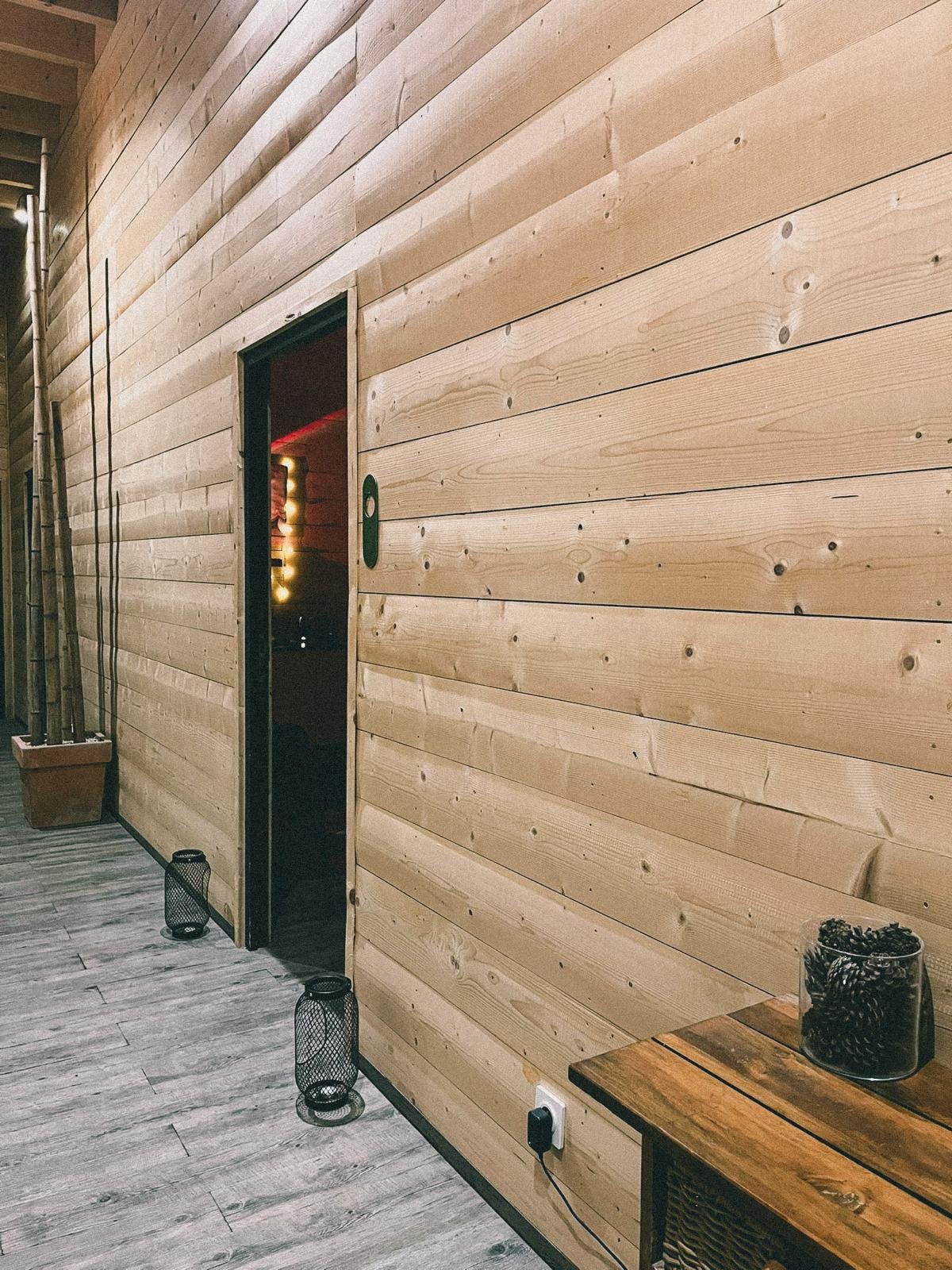 Mur en bois clair avec porte ouverte, deux lampes de table au sol, pot avec bambous, prise électrique et décoration à l'intérieur visible par l'ouverture.