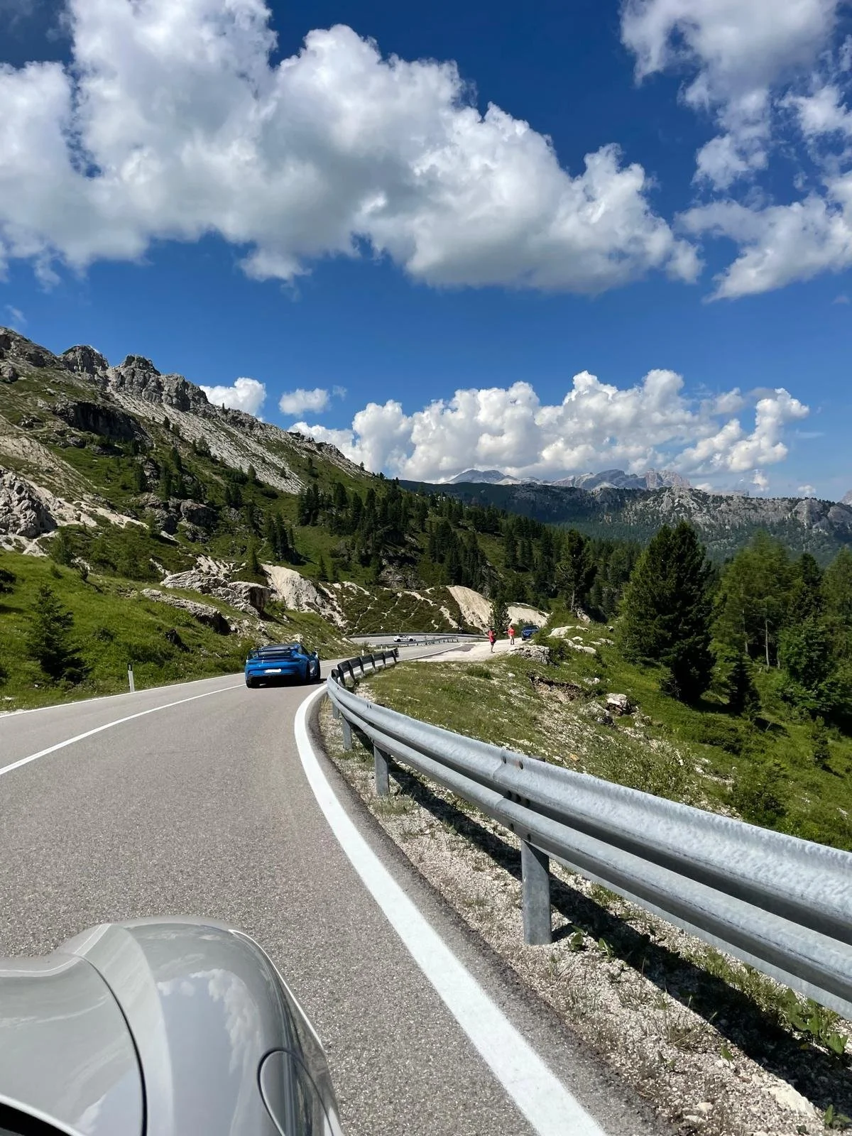 Kurvige Bergstraße mit Autos, grünen Bäumen, Felsen und Wolken am Himmel.