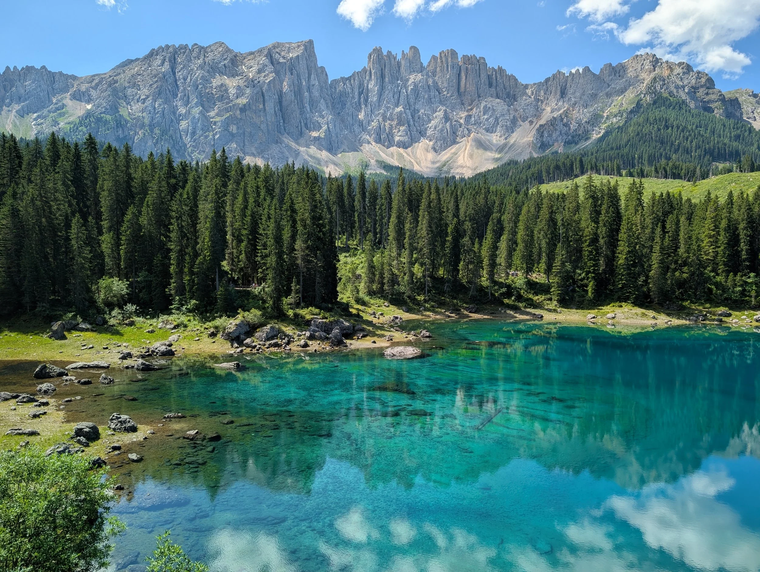 Bergsee mit klarer türkisfarbener Wasser, umgeben von grünen Wäldern und hohen Bergen im Hintergrund bei schönem Himmel.
