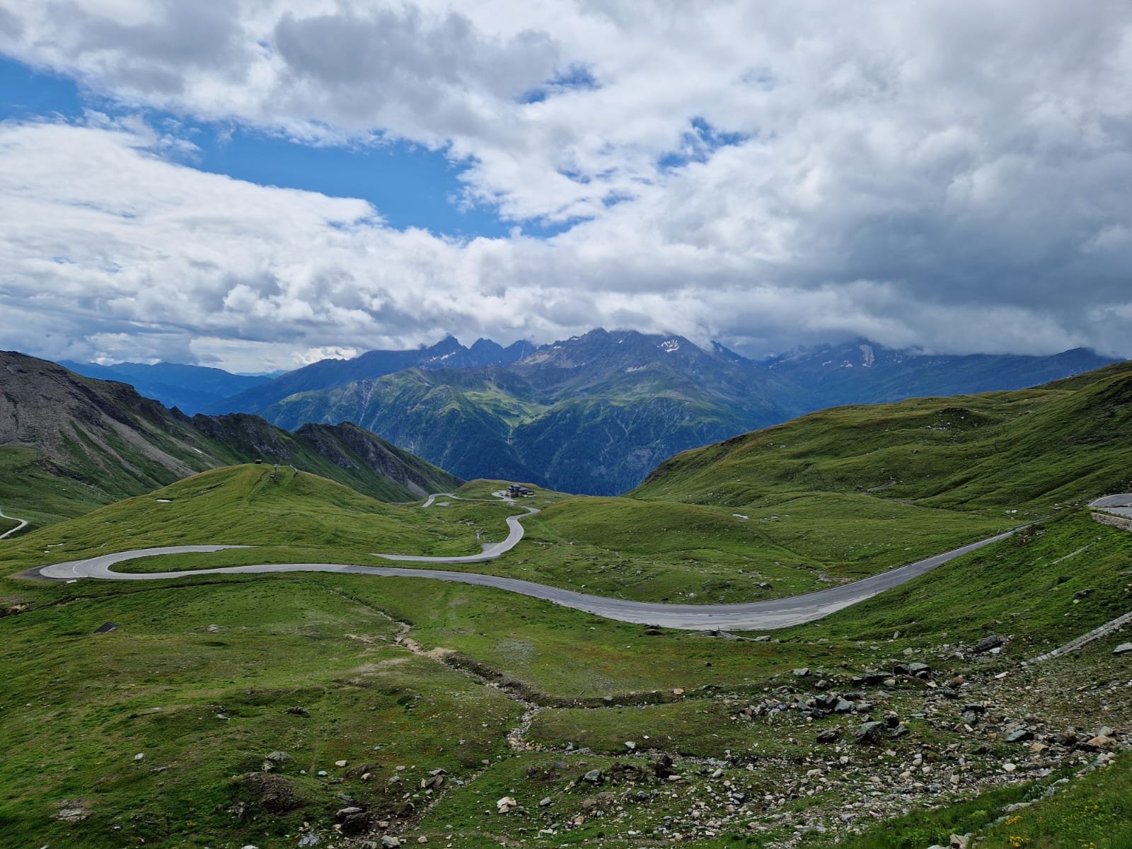 Berglandschaft mit kurvenreicher Straße und Wolken am Himmel.