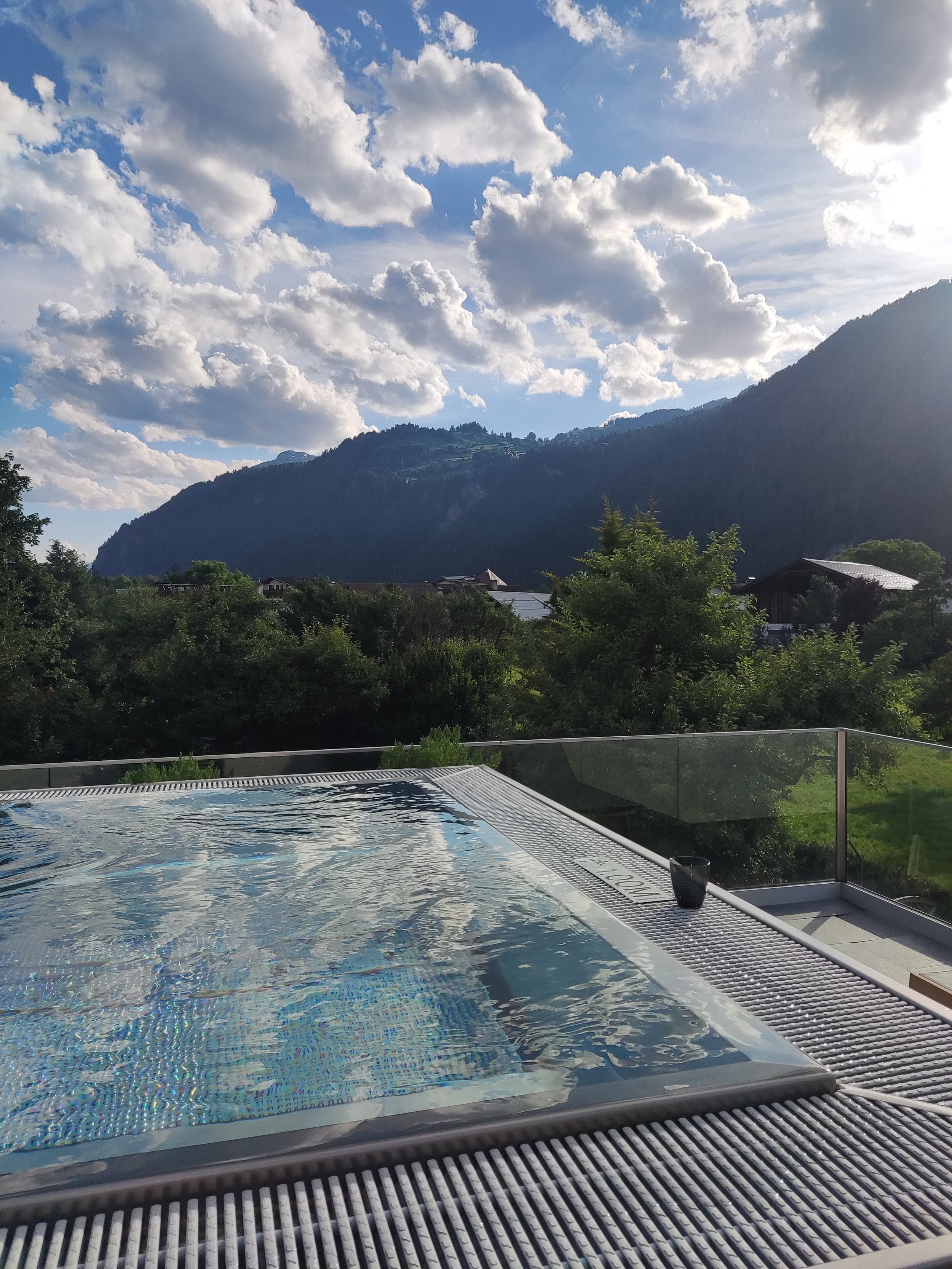 Oberer Blick auf einen Pool mit Blick auf grüne Hügel und Berge bei Sonnenuntergang unter einem bewölkten Himmel.