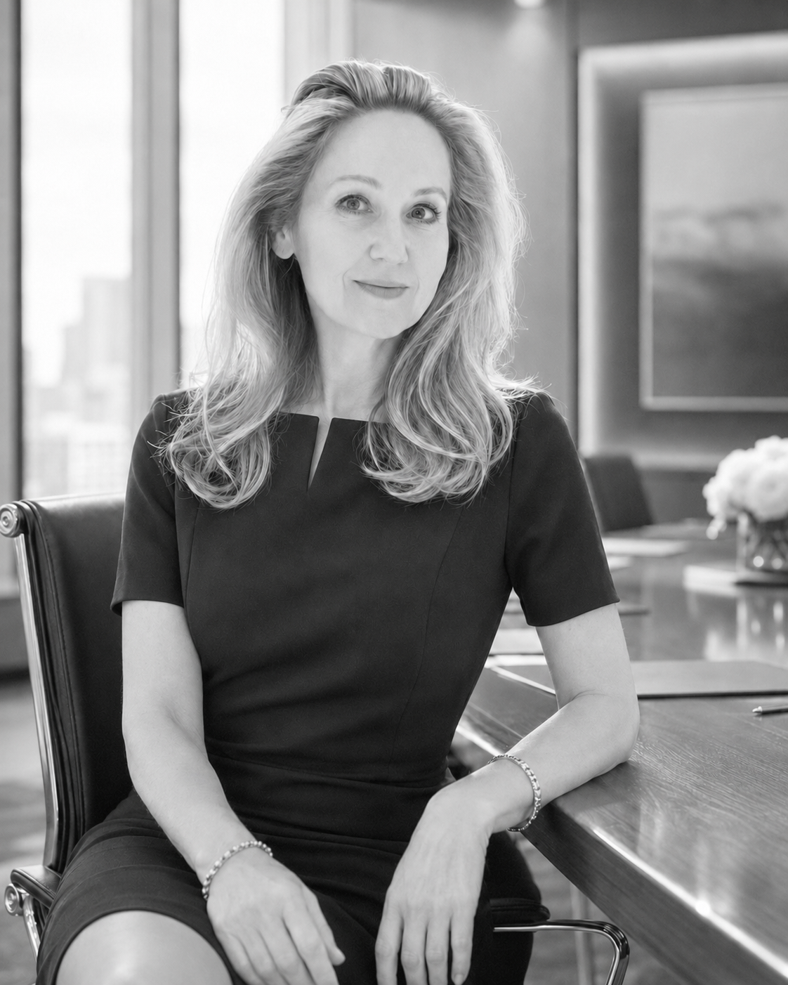 Josephine Dunn, Luxury Brand Strategist and Creative Consultant, sitting at a conference room table, wearing an elegant black dress, with a city view visible through the windows in the background.