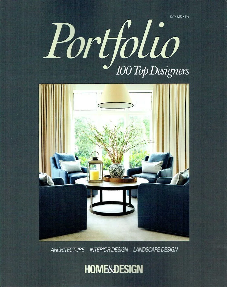 Kimmel Studio Architects 'Portfolio: 100 Top Designers' bright living room featuring four blue armchairs around a round wooden table with a plant, lantern, and candles, large window with beige curtains, and a modern hanging light fixture.