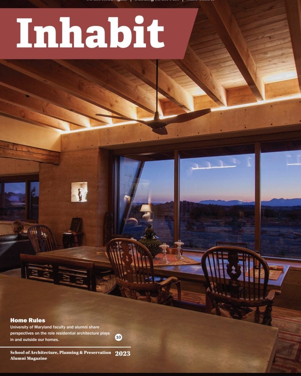 Kimmel Studio Architects Inhabit Magazine Interior of a house with a wooden ceiling, a ceiling fan, large windows showing a sunset landscape, and a dining table with chairs.