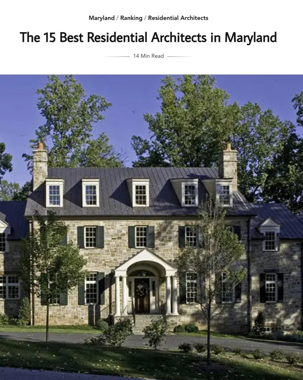 Kimmel Studio Architects large historic stone house with a metal roof, multiple dormer windows, front steps, and a portico with columns. Trees and a lawn are in the foreground, and a blue sky is above.