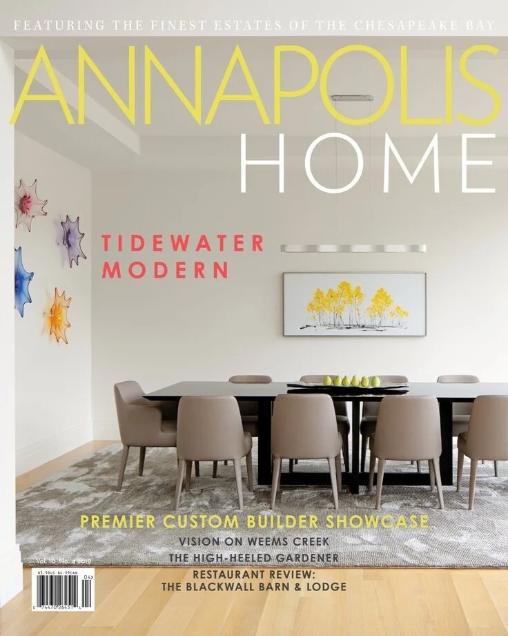 Kimmel Studio Architects Annapolis Home Magazine Modern dining room with a large table, beige chairs, a white wall with art, and text overlay promoting Annapolis home, Tidewater Modern, and local businesses.