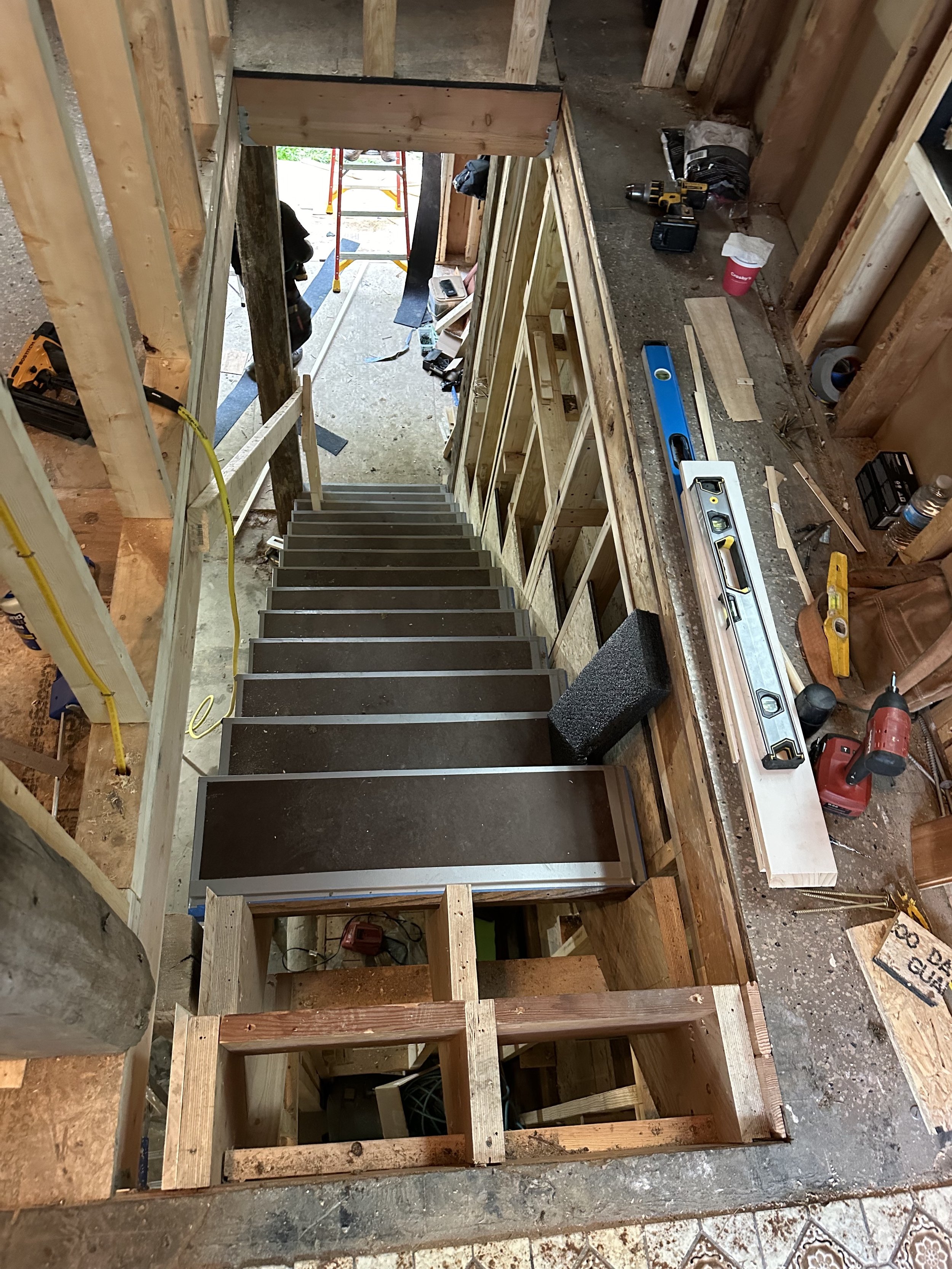 Construction site with a staircase under construction, surrounded by wooden framing, tools, and construction materials.