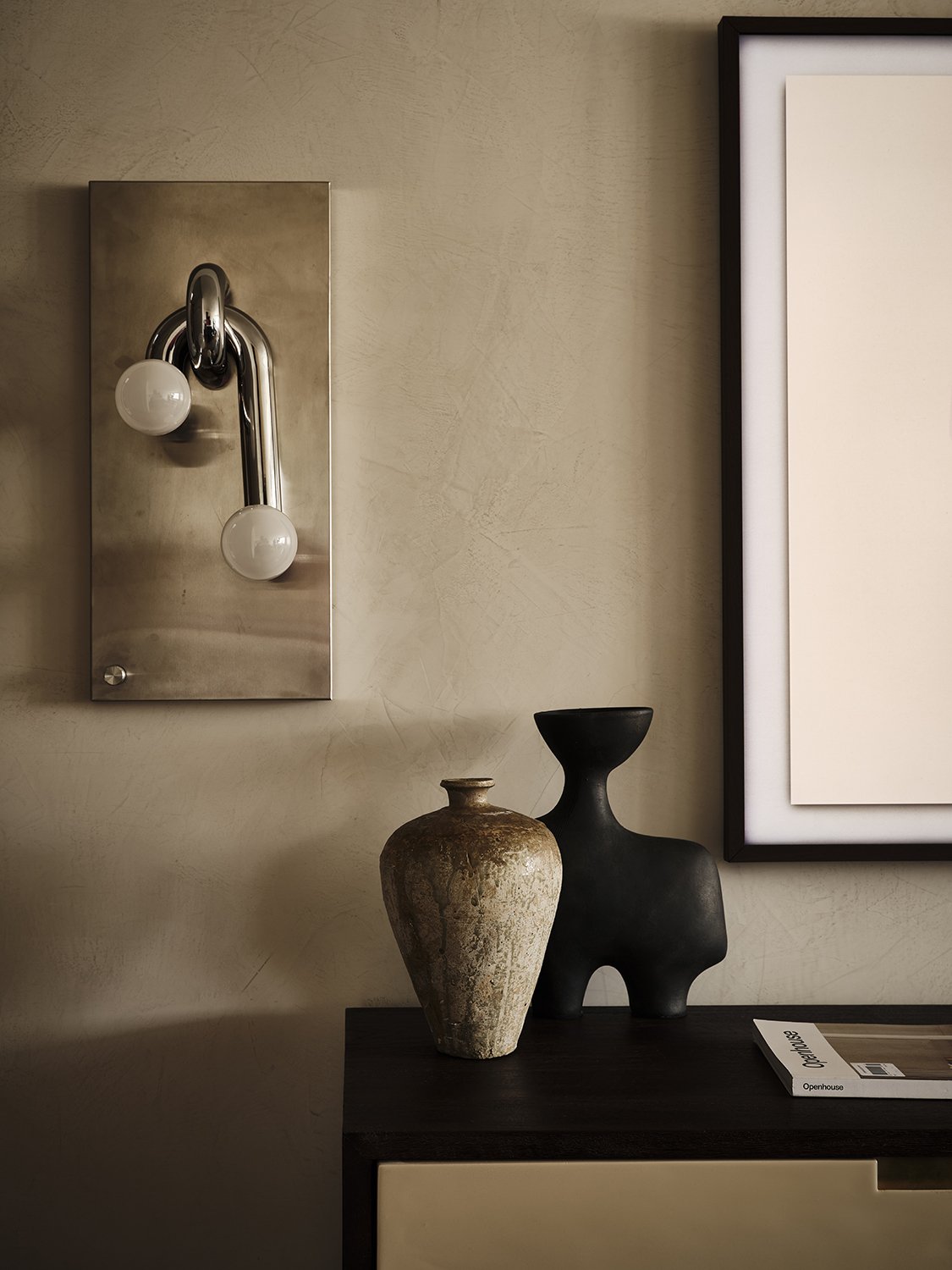 Interior wall decor with two vases on a dark table, and a modern wall light fixture with two bulbs.