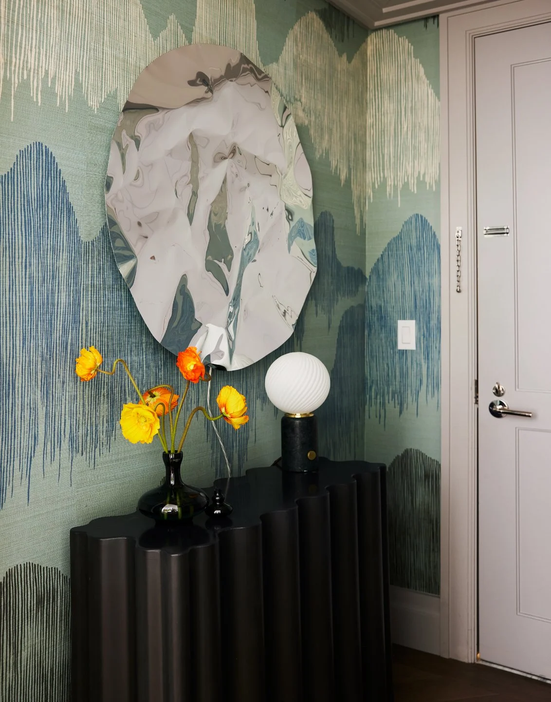 Accent wall with textured mural, black console table, decorative vases with yellow flowers, and a round white table lamp.