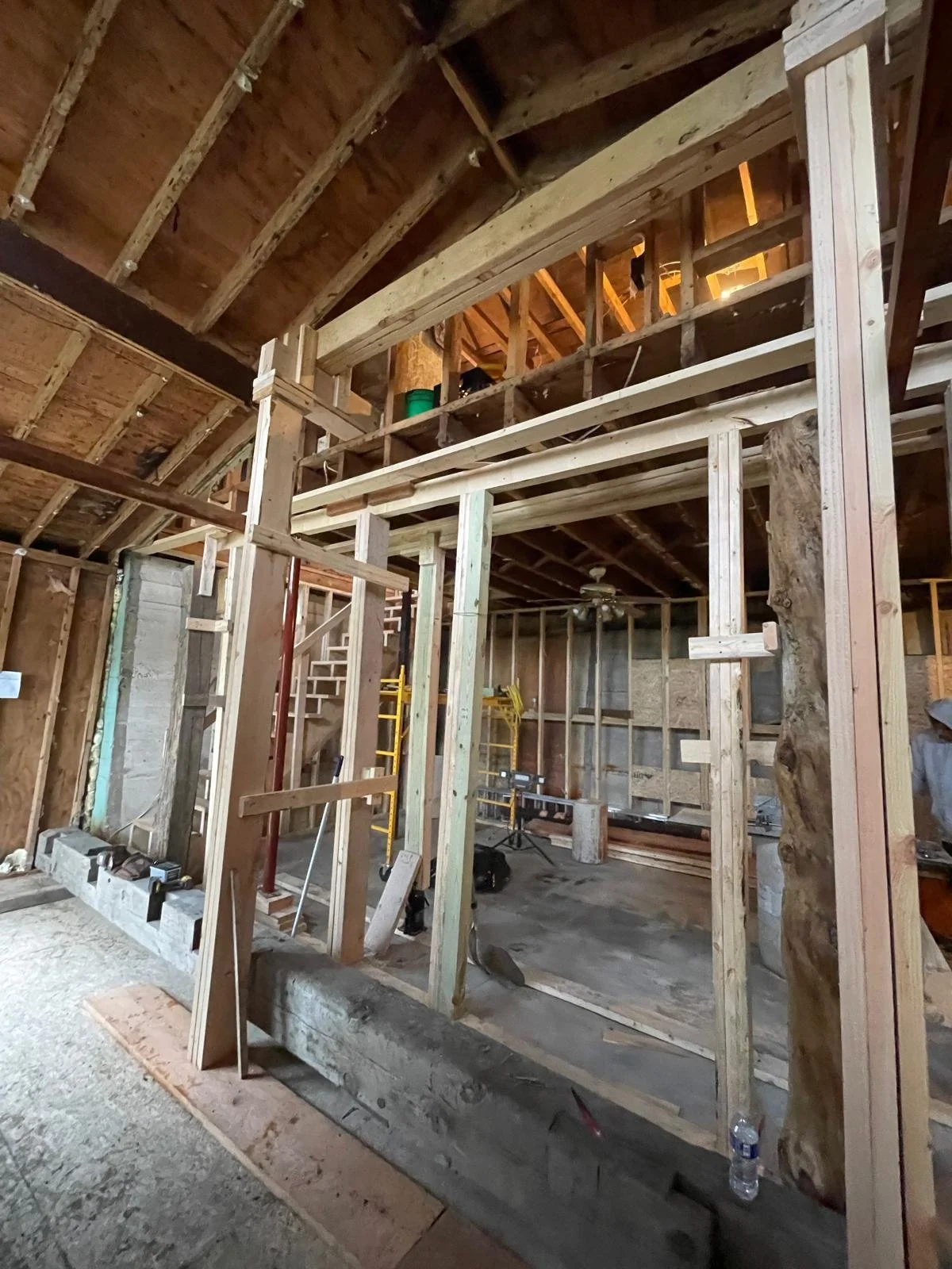 Interior view of a house under construction with wooden framing, stairs, and construction tools.
