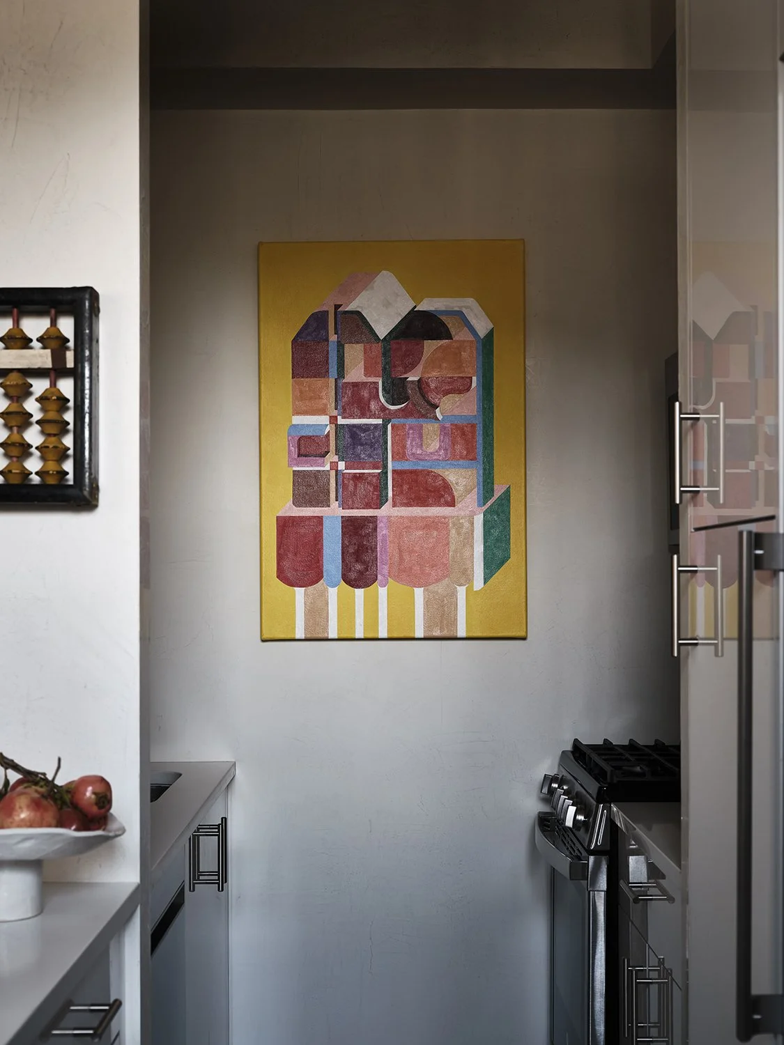 Colorful abstract geometric painting on kitchen wall with a bowl of apples on a counter to the left.